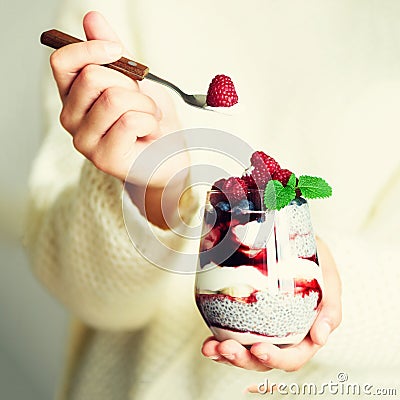 Girl in white sweater holds glass with chia milk dessert, raspberries, blueberries, mint. Healthy breakfast concept Stock Photo