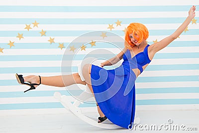 Girl wig rides swing little horse. Feel childish. Lady red or ginger wig blue dress rides rocking horse. Comic and Stock Photo