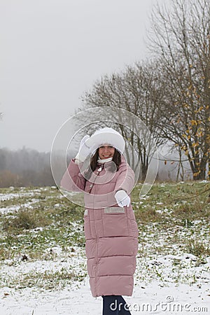 A girl in winter clothes on a walk in the park. Holds a ball of snow in his hand. The ground is covered with the first snow Stock Photo