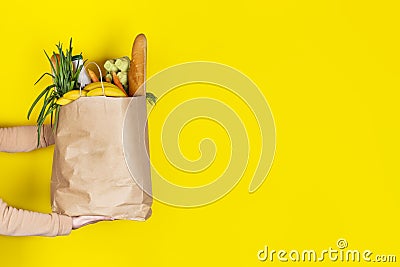 Girl or woman holds a paper bag filled with groceries such as fruits, vegetables, milk, yogurt, eggs isolated on yellow Stock Photo