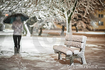Girl or woman walking on the strees with umbrella in snowstorm, bench with snow in the city, night photography Stock Photo