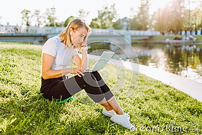 Girl working at the computer sittingon the grass in a protective medical mask on her face. Freelance, quarantine concept Stock Photo