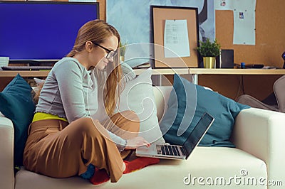 Girl works at home, sits on a sofa with a computer. Home schooling, online school. A girl looks at a computer, makes purchases Stock Photo