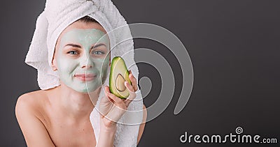 Girl wrapped in a towel with a cosmetic mask on her face and avocado in her hands Stock Photo