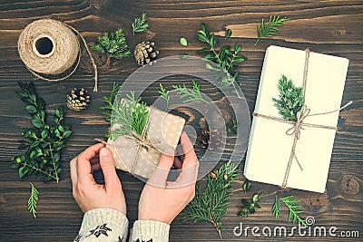 Girl wrapping christmas gift. Womans hands holding decorated gift box on rustic wooden table. Christmas DIY packing. Stock Photo
