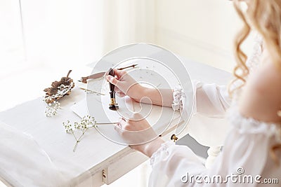 Girl writes a letter to her beloved man, sitting at home at table in a white light dress, purity and innocence. Curly blonde Stock Photo