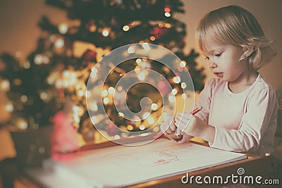 Girl writes a letter to Santa near the New Year tree at the table, soft focus Stock Photo