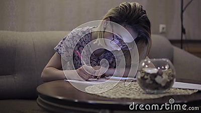 The girl writes in the notebook notes. Sitting in the living room at the table Stock Photo