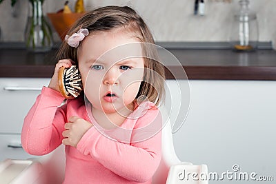 Girl 2 years old playing with a comb at home - portraying an emotional conversation on the phone. Stock Photo