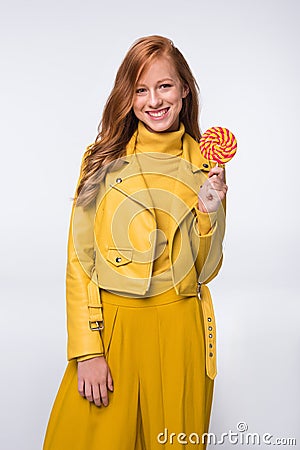 smiling redhead stylish girl in yellow leather jacket holdig lollipop Stock Photo