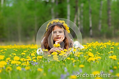 Girl with yellow wreath is laying in dandelions and violets in spring Stock Photo