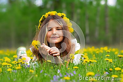 Girl with yellow wreath is laying in dandelions and violets in spring Stock Photo