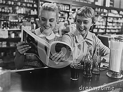 Girlfriends looking at magazine at soda fountain Stock Photo