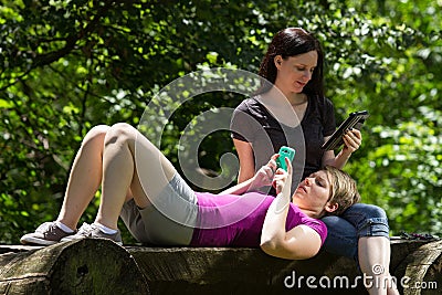 Girlfriends at park using smartphone and tablet, horizontal Stock Photo