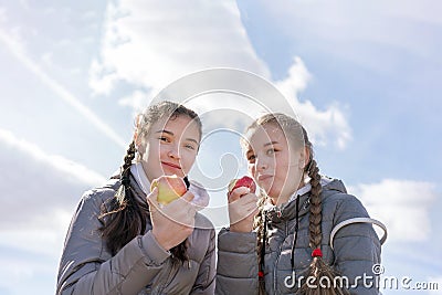 Girlfrinds with appetite bites off red apple sitting on bench Stock Photo