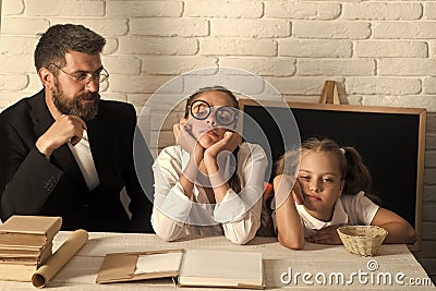 Girls and bearded man sit at desk with books Stock Photo
