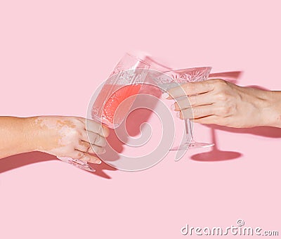 Girls cheers concept. Two woman hands, one with vitiligo hand holding vintage crystal glasses with lovely drinks in it against Stock Photo