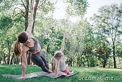 Girls are excercising in park. They are stretching together. Woman and kid are holding their left hand up and leaning to Stock Photo