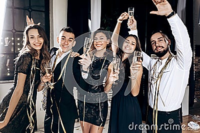 Girls and guys dressed in stylish elegant clothes having fun and clink glasses with champagne in the studio. Party time Stock Photo