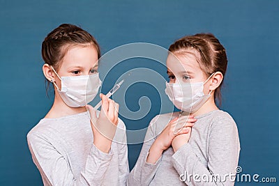 Girls in medical masks look at a syringe with medicine in their hands and are afraid. Vaccination, treatment of children. Stock Photo
