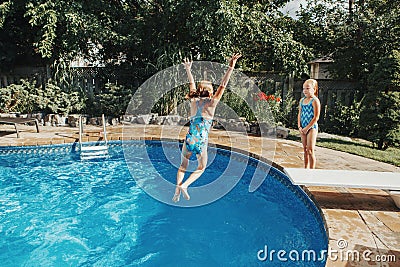 Girls sisters diving in water on home backyard pool. Children siblings friends enjoying and having fun in swimming pool together. Stock Photo