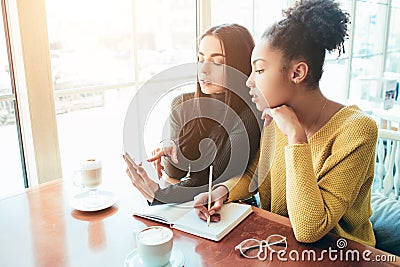 Girls sitting tigether very close to each other. One of them is writing something down in her notebook while the other Stock Photo