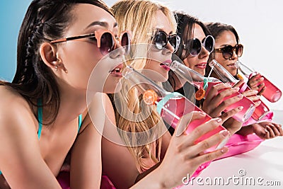 Girls in sunglasses drinking cocktails while sunbathing on swimming mattress Stock Photo