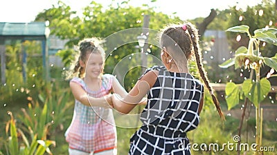 Girls teenagers whirl holding hands under the spray leading from a hose. Summer holidays, happy childhood stock footage Girls teenagers whirl holding hands under the spray leading from a hose. Summer holidays, happy childhood stock footage