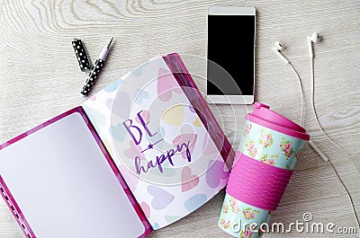 Girly thermos, notebook, phone and headphones on white wooden table Stock Photo