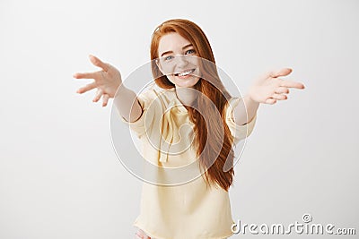 Give me warm hug. Studio shot of friendly cute redhead female student pulling hands towards camera, tilting head and Stock Photo