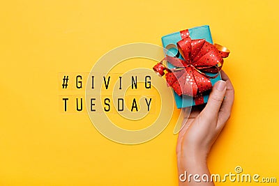Giving Tuesday. Global day of charitable giving after Black Friday shopping day. Woman hand holding gift box on yellow background Stock Photo