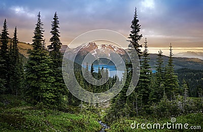 Glacial mountain Garibaldi lake with turquoise water in the middle of coniferous forest at sunset. View of a mountain lake between Stock Photo