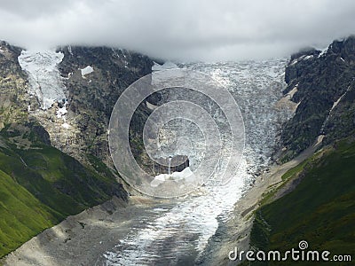 Glacier with nearby green lawns in the high Caucasus in Georgia. Stock Photo