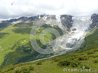 Glacier with nearby green lawns in the high Caucasus in Georgia. Stock Photo