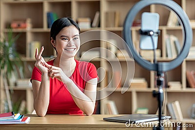 Glad asian teen chinese lady gesturing, shooting video for blog looking at smartphone in room interior Stock Photo
