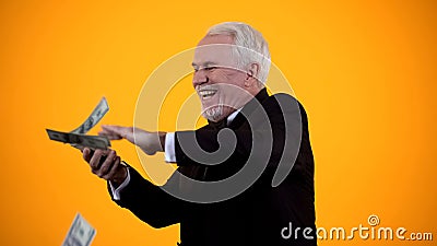 Glad elderly person in suit throwing dollar notes and smiling, good income, win Stock Photo