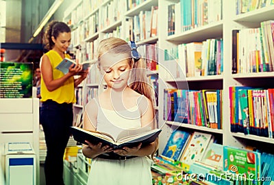 Glad girl in school age looking in open chosen book Stock Photo