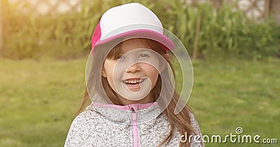 Glad liten söt flicka i lastbilschaufförer som leker och tittar på kameran medan man står i sommarträdgård stock video Glad liten söt flicka i lastbilschaufförer som leker och tittar på kameran medan man står i sommarträdgård stock video