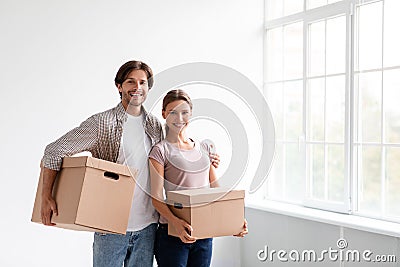 Glad millennial caucasian man and woman in casual carry boxes, hugs and enjoy renting new flat in empty room Stock Photo