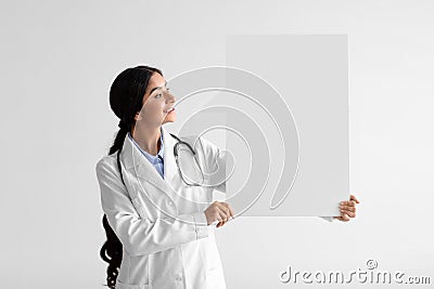 Glad pretty young hindu woman doctor in white coat with stethoscope hold large abstract empty space for words Stock Photo