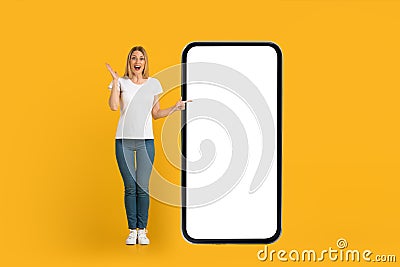 Glad shocked young european woman with open mouth in white t-shirt points finger at huge phone with blank screen Stock Photo