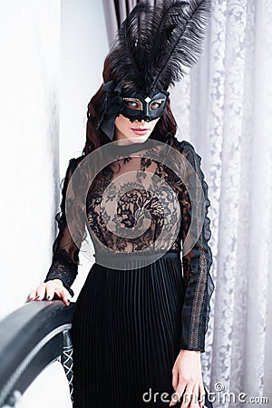Glamorous brunette lady with a beautiful hairstyle and red lips, in an evening dress, a Venetian black mask with stylish accessori Stock Photo