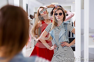 Glamorous girls trying on sunglasses posing in front of the mirror in fashion boutique Stock Photo