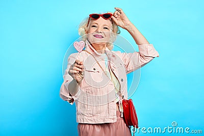 Glamour awesome blonde senior lady taking off sunglasses, while eating lollipop Stock Photo