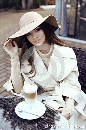 Glamour girl with dark straight hair wears luxurious beige coat with elegant hat, Stock Photo
