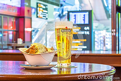 Glass of beer Heineken and plate of breadcrumbs and cheese. In the background, online board displays flights to the airport. Russi Editorial Stock Photo