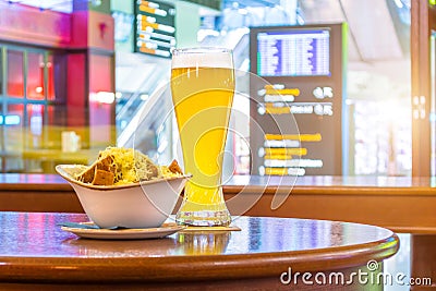 A glass of beer and a plate of breadcrumbs and cheese. In the background, online board displays flights to the airport. Concept ex Stock Photo