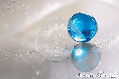 Glass blue ball on a white glass table. Abstract photo with glass and reflection. Stock Photo