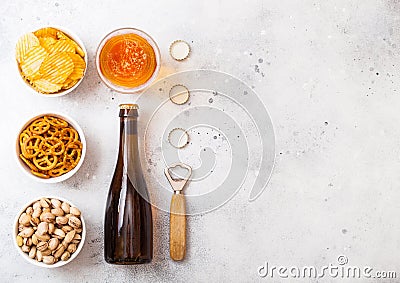 Glass and bottle of craft lager beer with snack and opener on stone kitchen table background. Pretzel and crisps and pistachio in Stock Photo