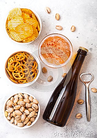 Glass and bottle of craft lager beer with snack and opener on stone kitchen table background. Pretzel and crisps and pistachio in Stock Photo